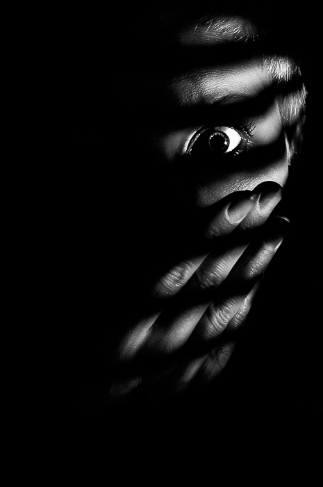 Low key concept photo of woman looking through window jalousies